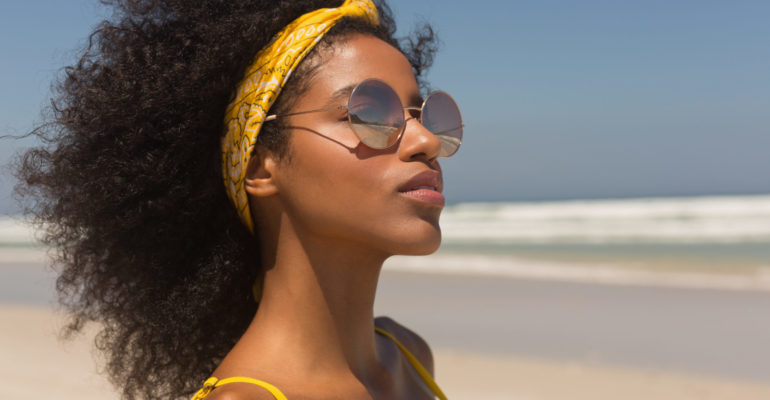Young African American woman in yellow bikini and sunglasses sta